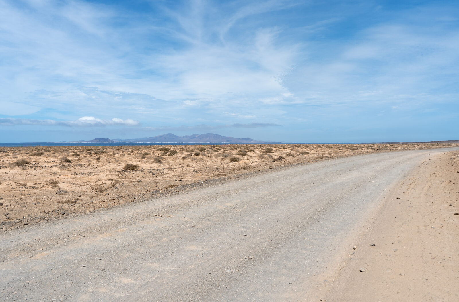 Empty coastal road between Corralejo and El Cotillo in northern Fuerteventura, low-rolling open volcanic terrain typical of the FV roads