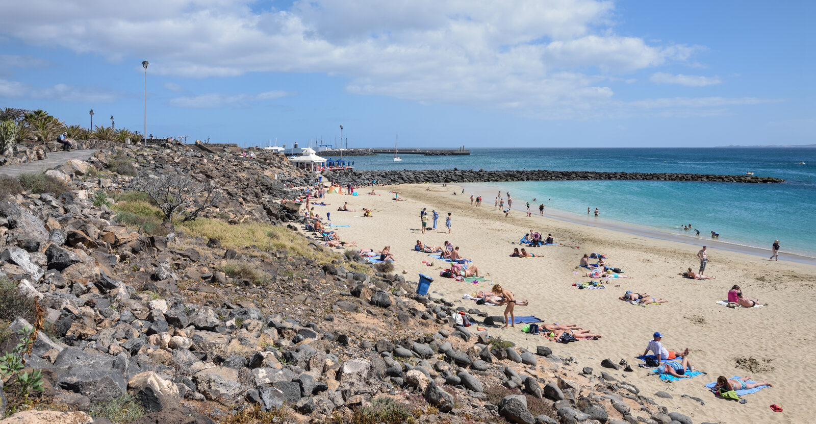 Sandy beach in Playa Blanca, southern Lanzarote, with low-rise buildings along the shoreline and Marina Rubicón visible in the distance