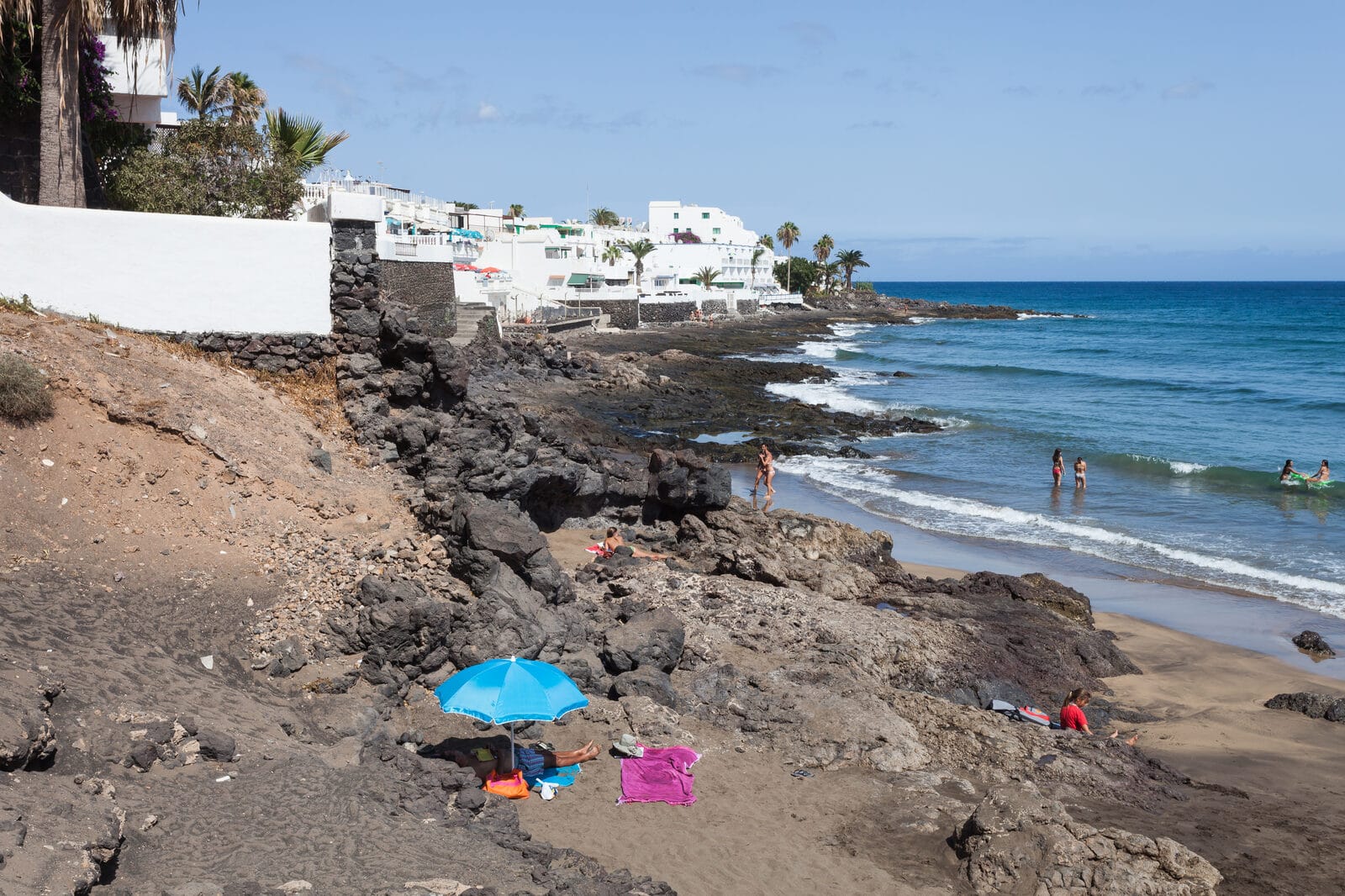 Playa Grande in Puerto del Carmen, Lanzarote, with sunbeds and parasols on dark sand and clear water
