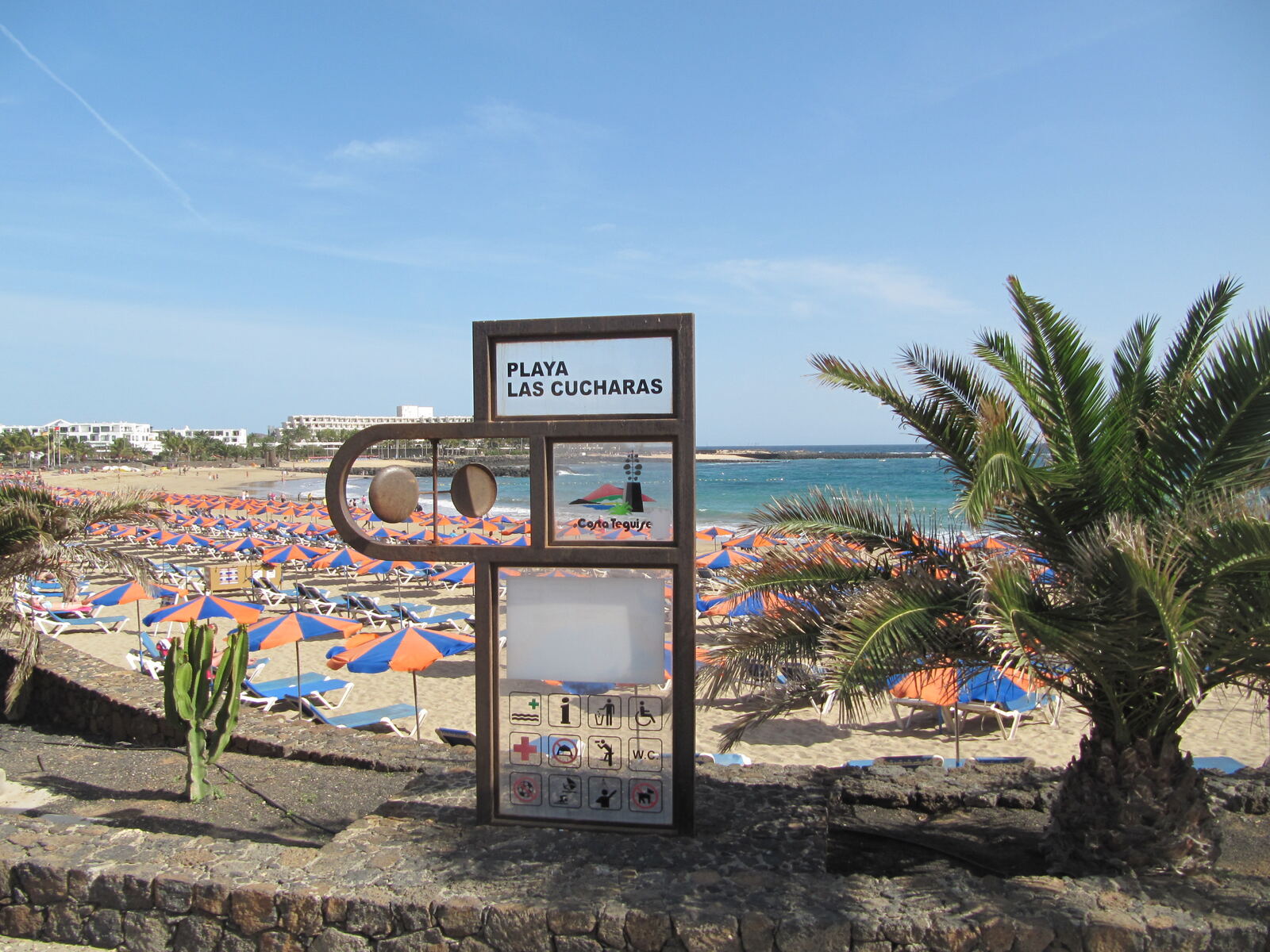 Playa Las Cucharas sign in Costa Teguise, Lanzarote, with orange beach umbrellas behind