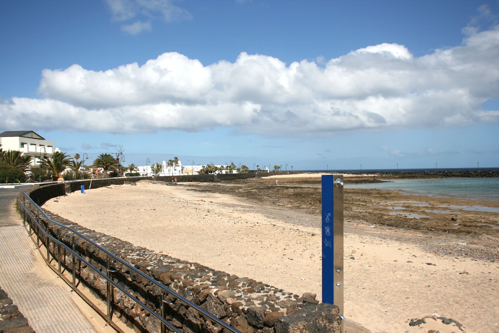 Playa de Los Charcos in Costa Teguise, Lanzarote, sandy beach with a volcanic rock reef exposed at low tide and breakwater behind