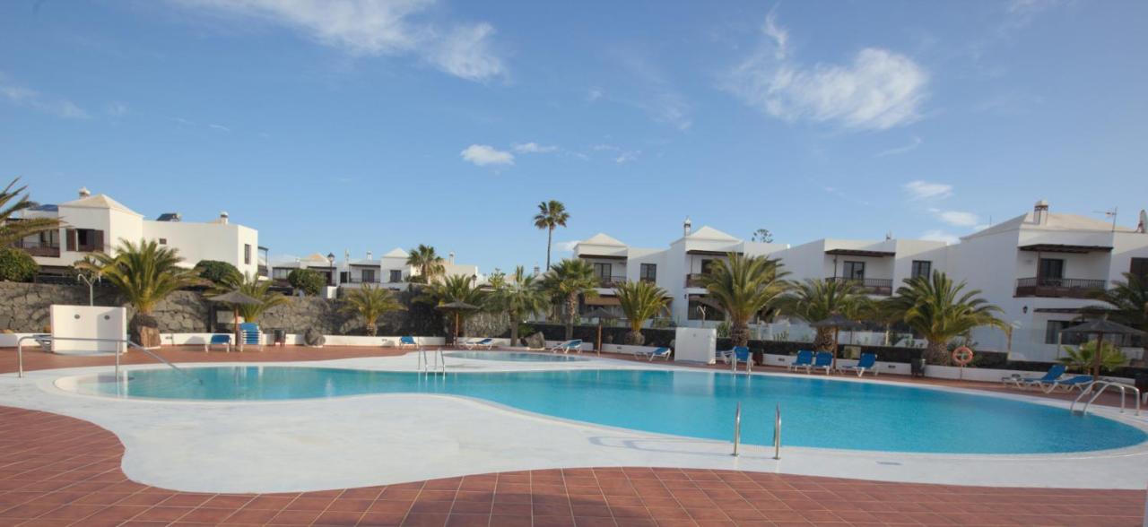 Swimming pool with palm trees and white villas in Costa Teguise